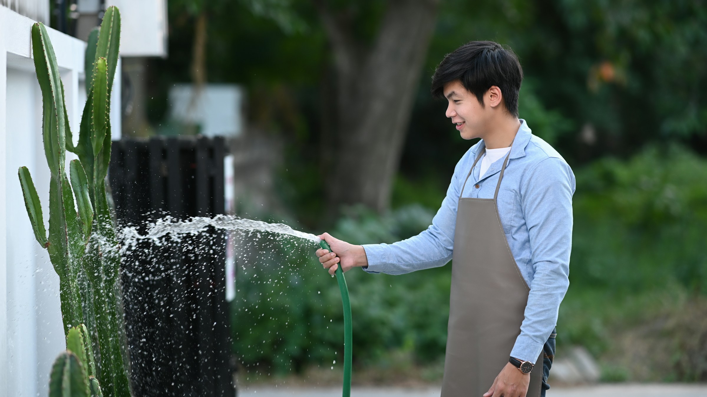 A person wearing an apron waters plants with a hose in a garden setting, applying nutrients through EZ-FLO fertigation.