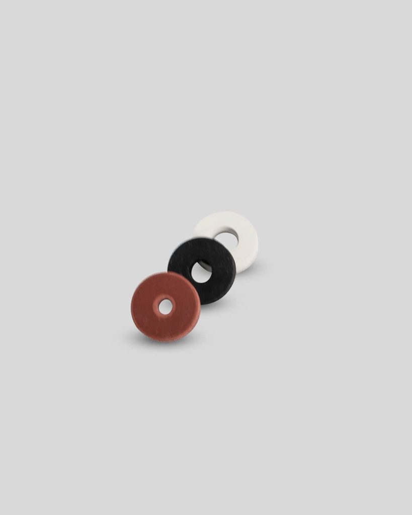 Three flat, round washers—one red, one black, and one white—are arranged in a diagonal line on a plain light gray background, perfect for your Import placeholder,2950 needs.